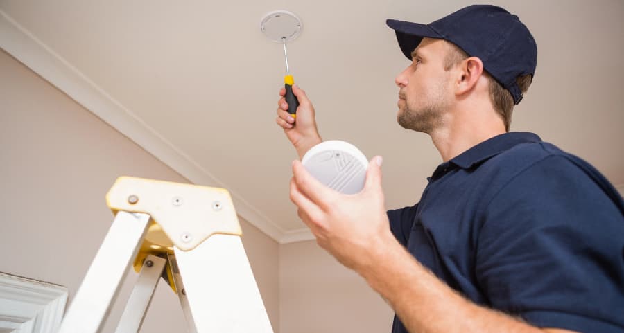 Man putting smoke alarm on ceiling of home